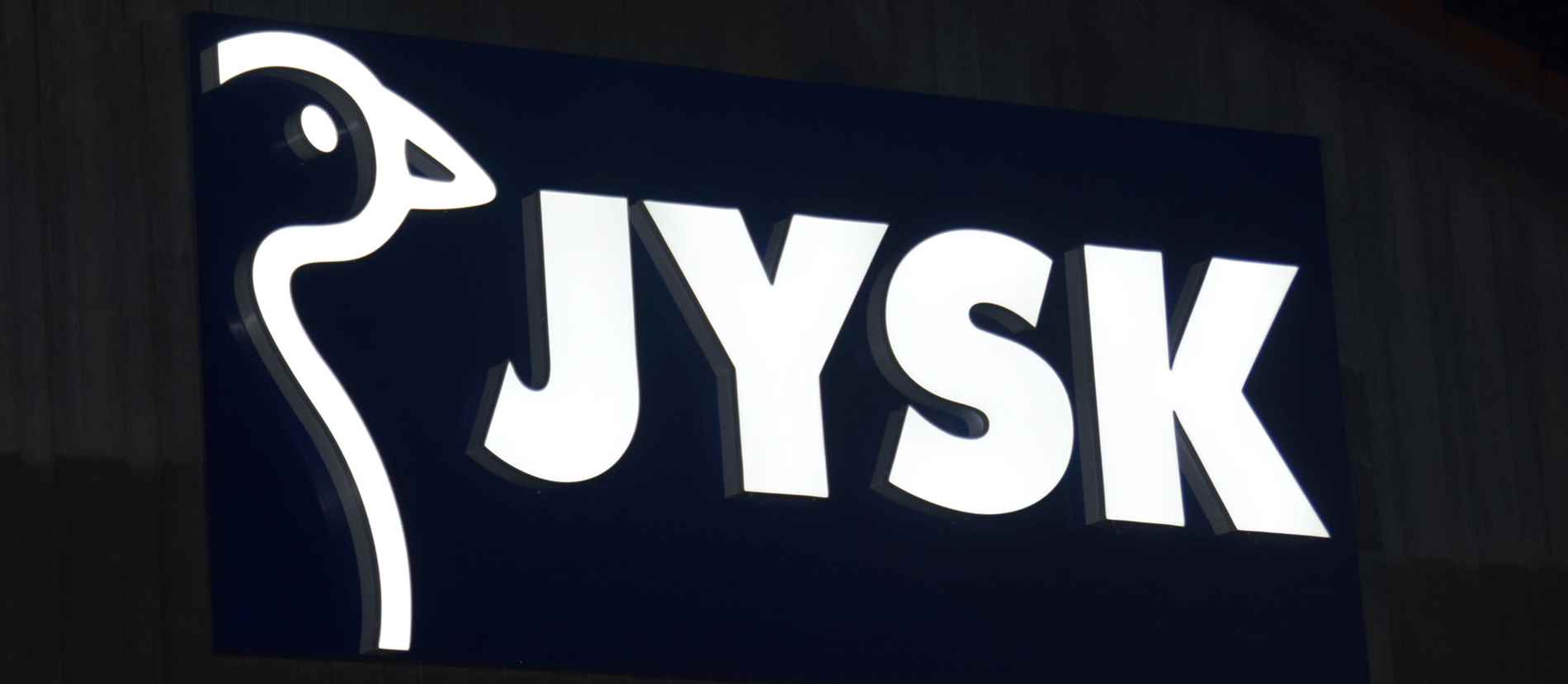 Leuchtendes JYSK-Logo an der Fassade eines Geschäfts in Freystadt. Das moderne Rebranding und die klare, helle Beleuchtung des Logos machen das Geschäft auch bei Nacht gut sichtbar und ziehen Kunden an.