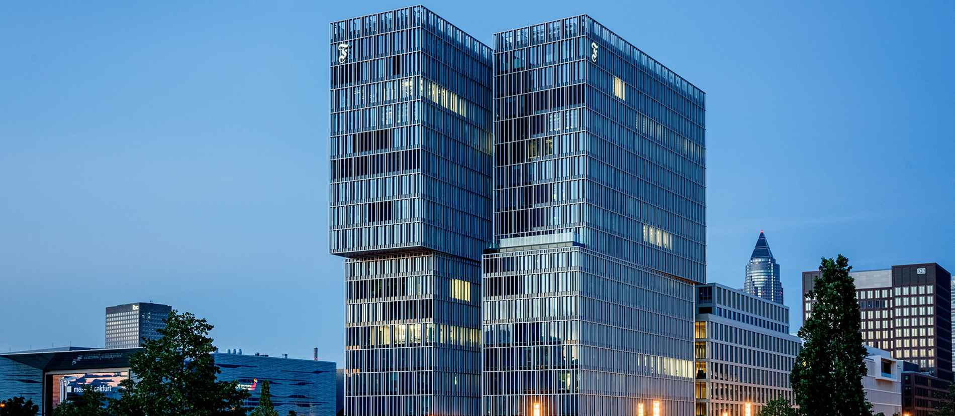 Moderne Hochhäuser bei Dämmerung in Frankfurt. Die beeindruckende Architektur der Gebäude wird durch hochwertige Leuchtbuchstaben und Lichtwerbung betont. Diese stilvolle Beleuchtung verleiht der Skyline von Frankfurt ein markantes und professionelles Aussehen.