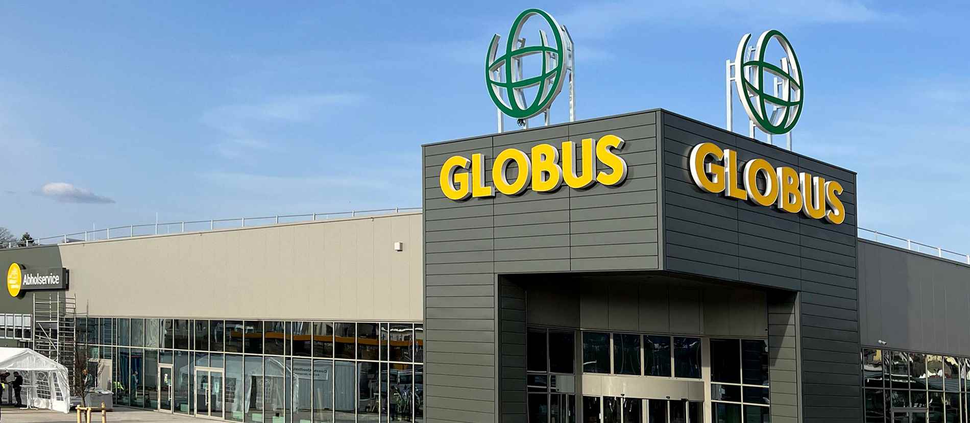 Globus-Markt in Neunkirchen mit großer, effizienter Lichtwerbeanlage. Die leuchtenden, gelben Globus-Schriftzüge und das markante grüne Logo machen den Eingangsbereich des modernen Einkaufszentrums gut sichtbar und einladend.